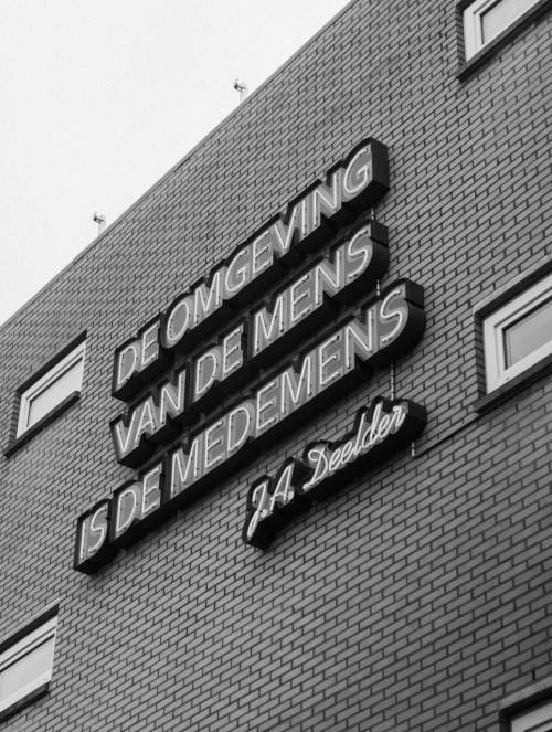 Quote J.A. Deelder 'De omgeving van de mens is de medemens' op een gebouw in de Nieuwe Binnenweg in Rotterdam.